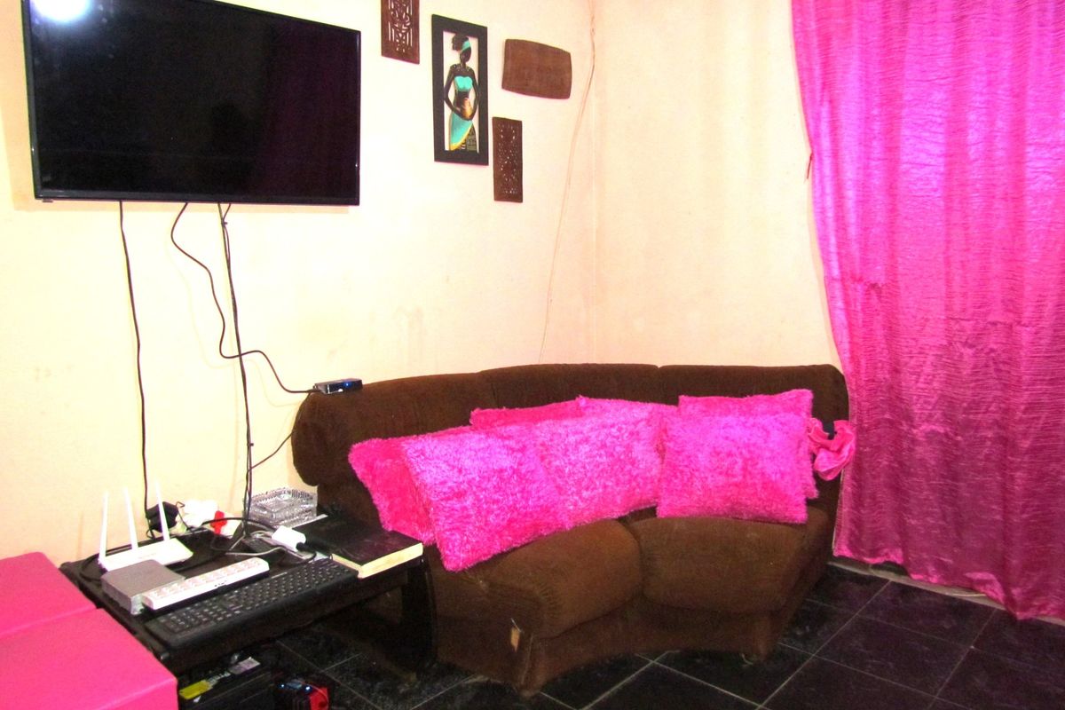 A living room area featuring dark floor tiles and wall-mounted television, requiring cosmetic updates to the wall finishes and cable management.