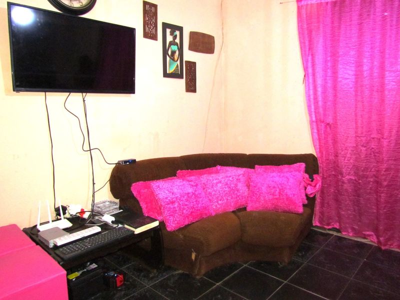 A living room area featuring dark floor tiles and wall-mounted television, requiring cosmetic updates to the wall finishes and cable management.