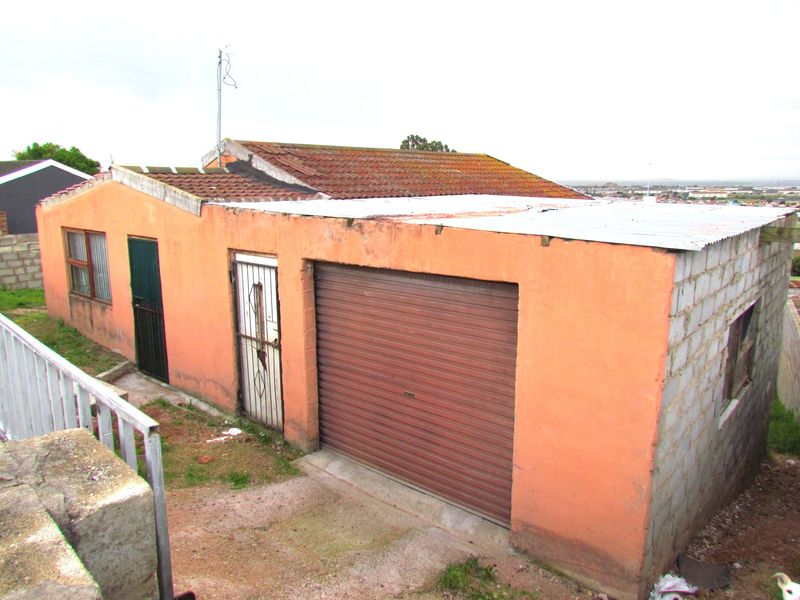 Exterior view of a detached garage featuring a roller shutter door, security gate, and concrete block construction with a tiled and metal roof.