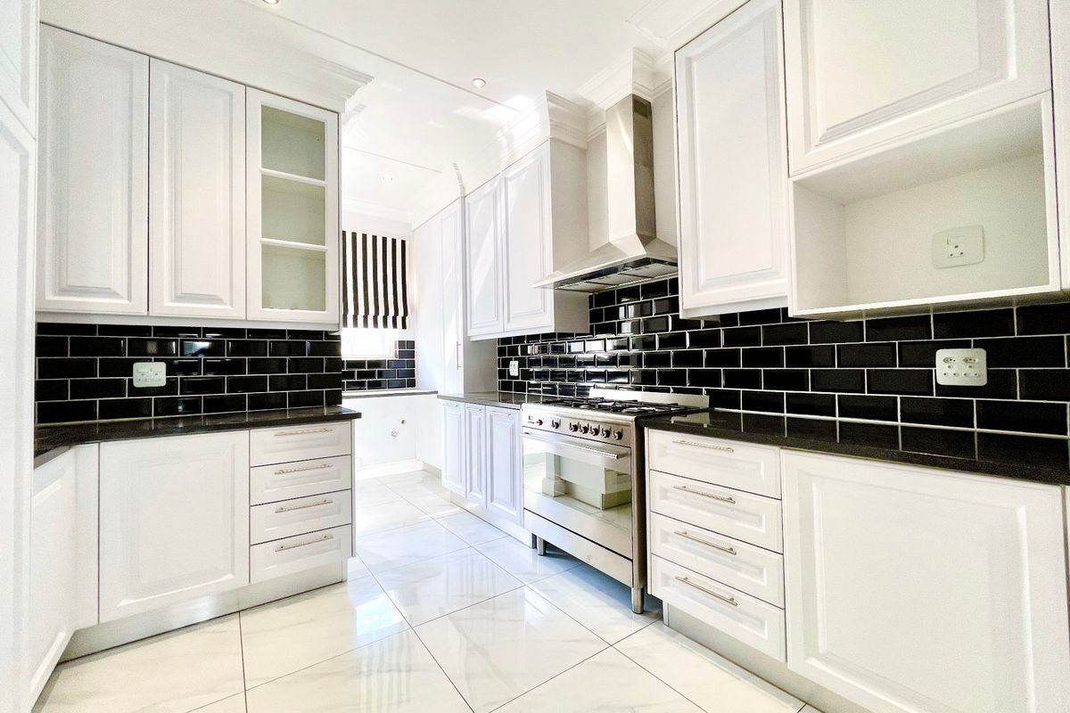 Modern kitchen featuring white shaker cabinetry, black subway tile backsplash, granite countertops, and a stainless steel gas stove with extractor fan.