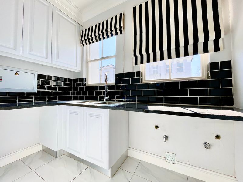 A clean and functional scullery featuring white cabinetry, black granite countertops, and a striking black subway tile backsplash with dedicated plumbing connections.