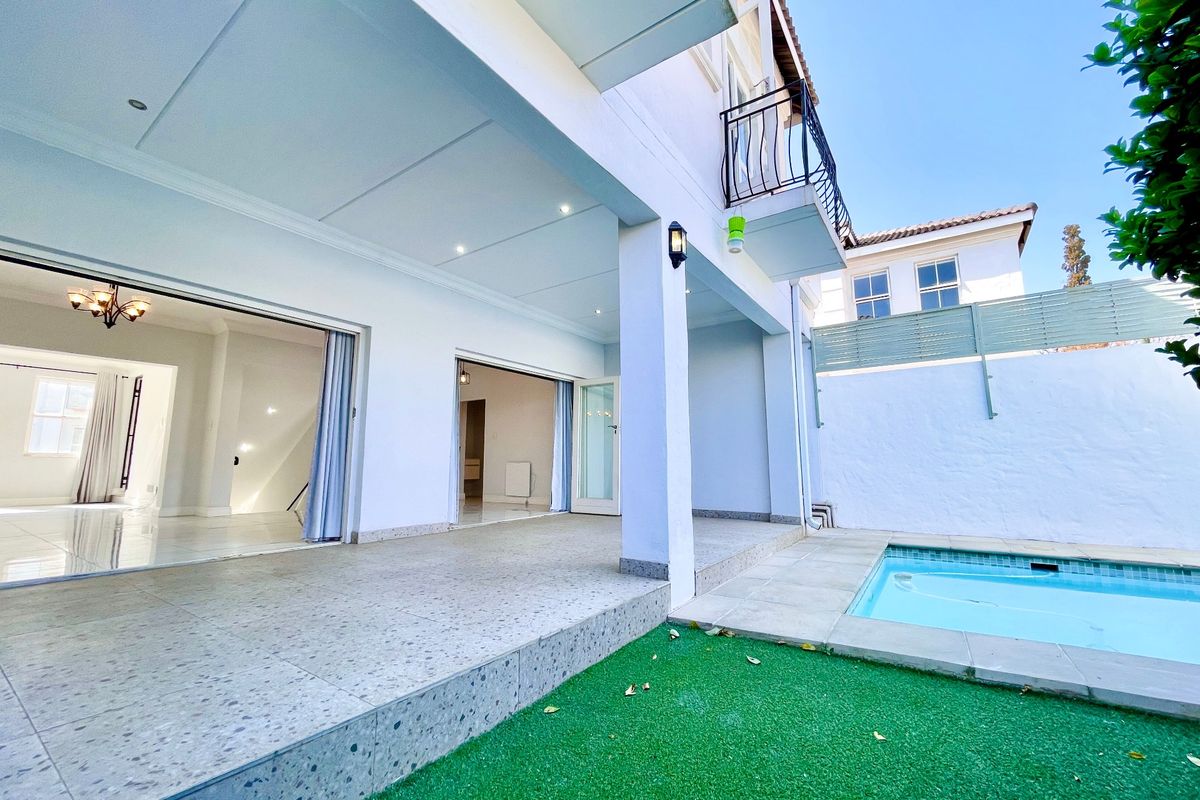 Rear exterior view featuring a covered patio, swimming pool, artificial lawn, and direct access to the interior living spaces through sliding glass doors.