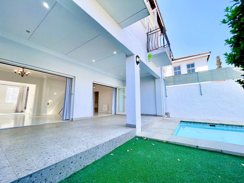 Rear exterior view featuring a covered patio, swimming pool, artificial lawn, and direct access to the interior living spaces through sliding glass doors.