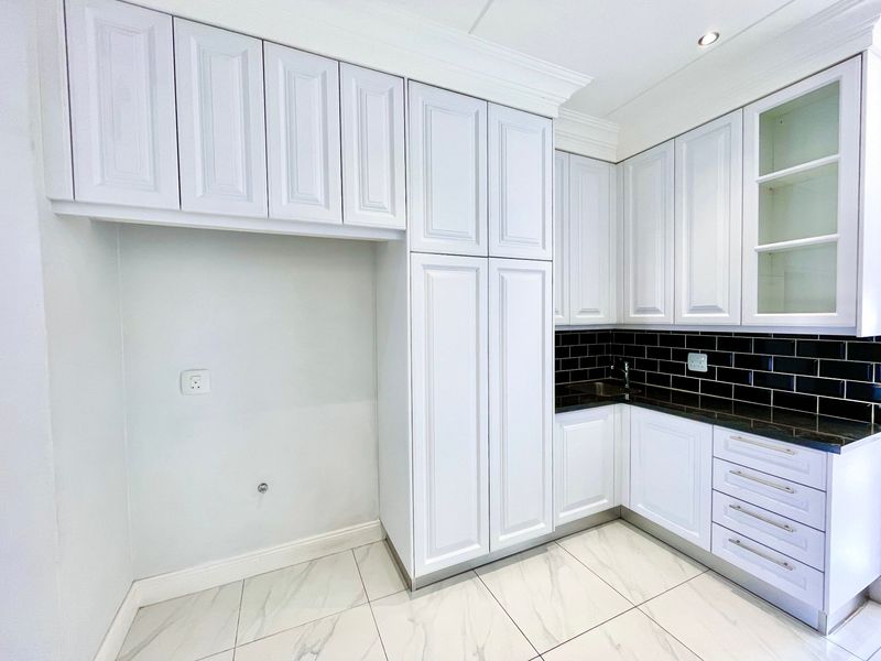 A clean, modern kitchen featuring white shaker-style cabinetry, contrasting black subway tile backsplash, dark granite countertops, and elegant marble-look floor tiles.