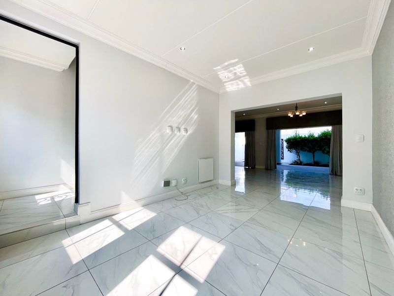 Bright and spacious open-plan living area featuring polished marble-look floor tiles, recessed lighting, and elegant ceiling cornicing, leading to an outdoor patio space.