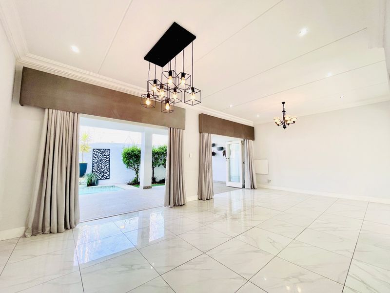 Spacious, light-filled living area featuring polished marble-look floor tiles, modern lighting fixtures, and seamless access to the outdoor patio and pool area.