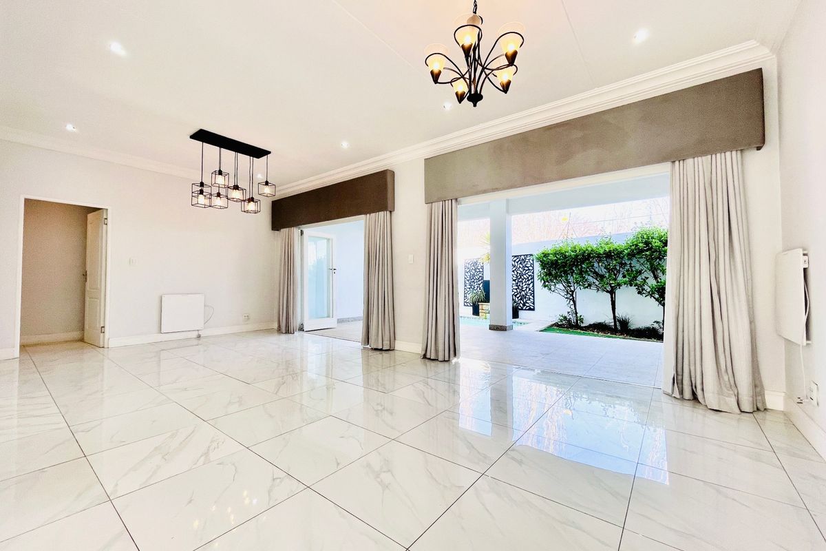 Spacious, light-filled living area featuring polished marble-look floor tiles, elegant chandeliers, and large sliding doors opening onto a covered patio and garden.