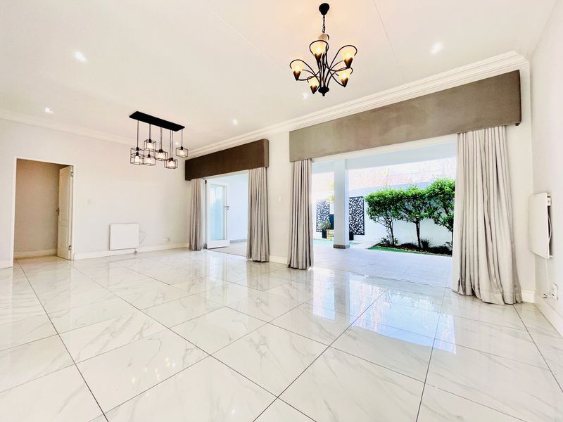 Spacious, light-filled living area featuring polished marble-look floor tiles, elegant chandeliers, and large sliding doors opening onto a covered patio and garden.