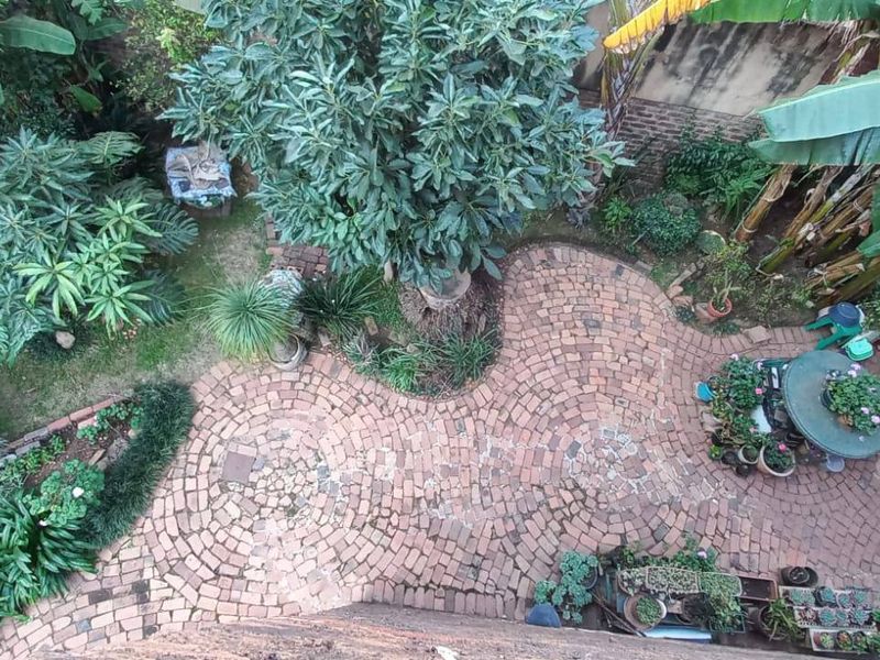 An elevated view of a private garden featuring a curved brick-paved courtyard, mature trees, and established landscaping enclosed by a brick boundary wall.