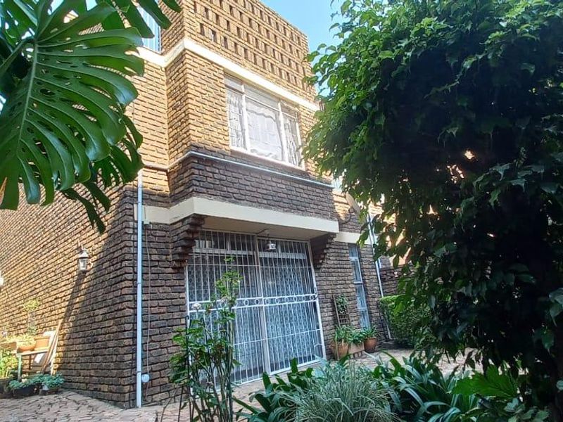 Rear view of a face brick townhouse featuring a paved patio area and established garden surroundings.