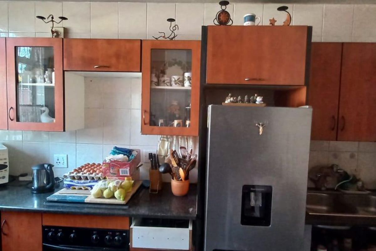 A dated kitchen featuring wood-look laminate cabinetry, tiled backsplash, and dark countertops, currently showing signs of wear including a missing drawer front.
