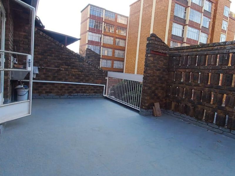 An open-air balcony featuring exposed brick walls, a metal safety railing, and painted concrete flooring, offering a functional outdoor space.