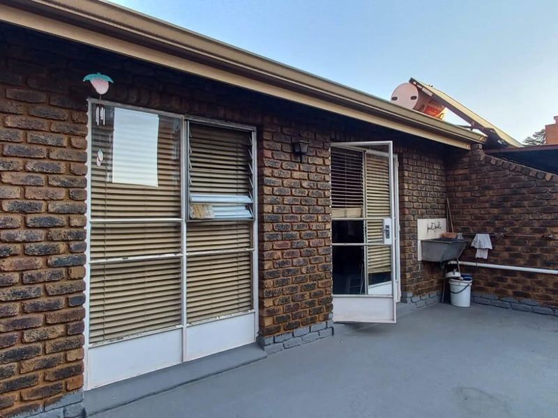Rear exterior view of the townhouse featuring exposed brick walls, a concrete patio area, and a functional utility sink.