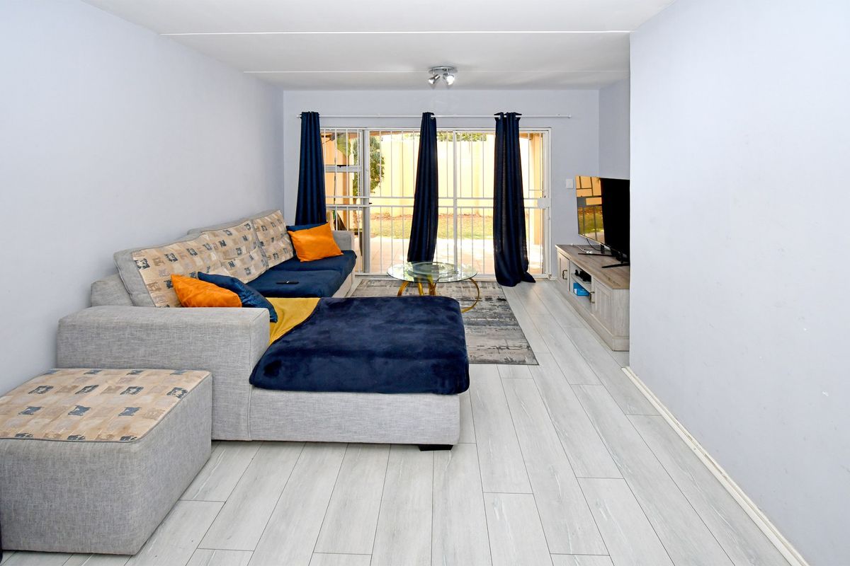 A bright living room featuring light-toned laminate flooring and a sliding glass door with security gate providing access to the outdoor area.
