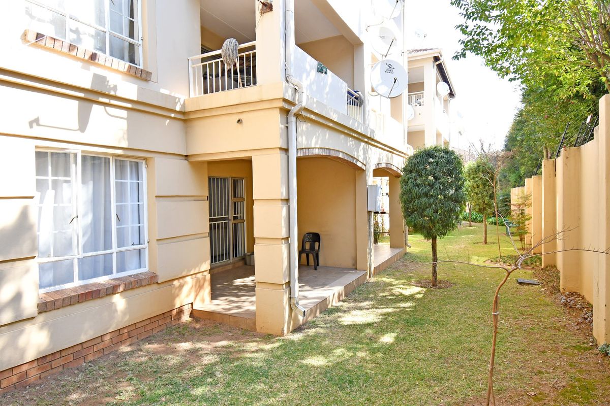Rear view of the apartment building featuring a covered ground floor patio, upper-level balcony, and access to a shared garden area.