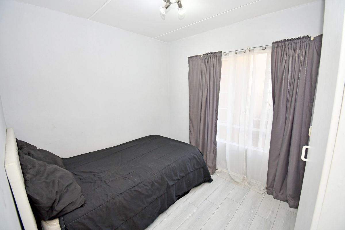 A compact bedroom featuring light-toned laminate flooring and a window with curtain treatments.