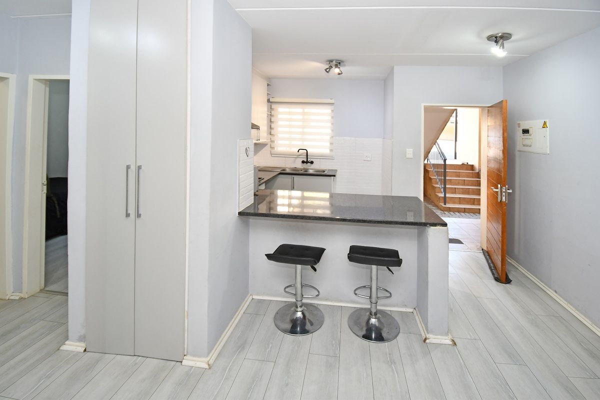 A compact kitchen featuring a granite breakfast bar, built-in cabinetry, and a double sink, with direct access to the apartment entrance.