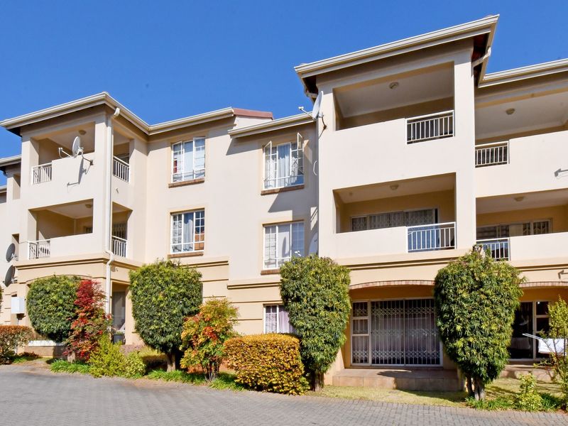 Front elevation of a multi-story apartment complex featuring private balconies, paved driveway access, and established garden landscaping.