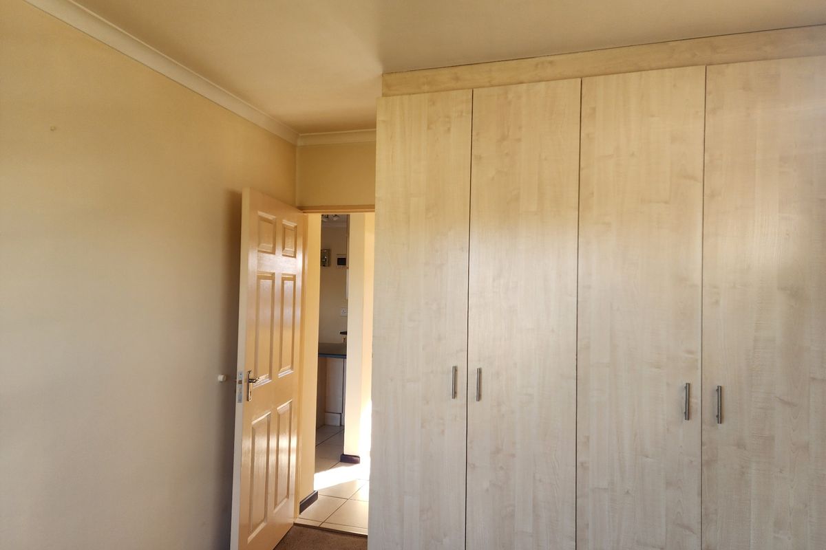 A bedroom featuring light wood-finish built-in cupboards, neutral wall paint, and coving, with an open doorway leading to an adjacent tiled area.