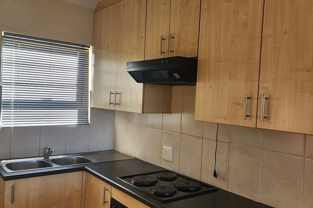 A functional kitchen featuring light wood-finish cabinetry, a double stainless steel sink, tiled splashbacks, and a built-in electric hob with an extractor fan.