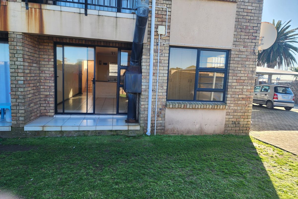 Rear view of a face brick townhouse featuring a tiled patio, sliding glass door access, and an external fireplace flue.