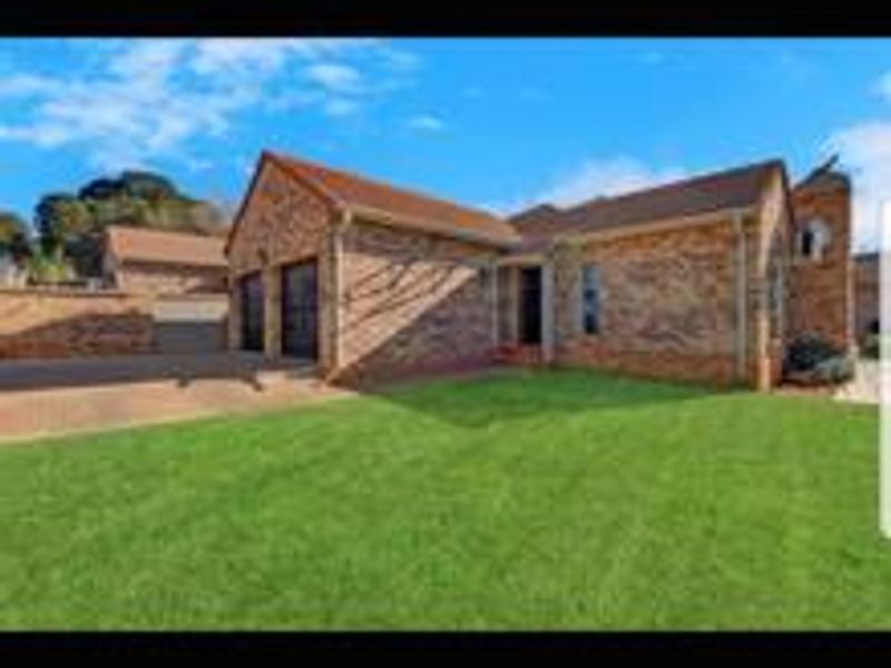 Front exterior view of a face-brick cluster home featuring a double garage, paved driveway, and a well-maintained lawn.