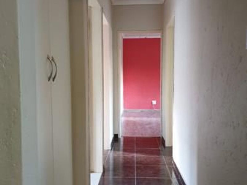 A clean, empty hallway featuring tiled flooring and built-in storage cupboards, leading towards a room with a red accent wall.