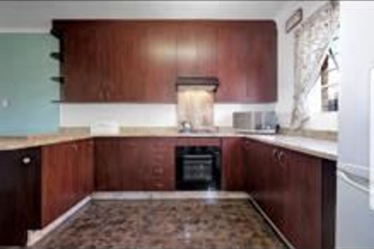 A U-shaped kitchen featuring dark wood cabinetry, integrated oven and hob, and stone countertops.