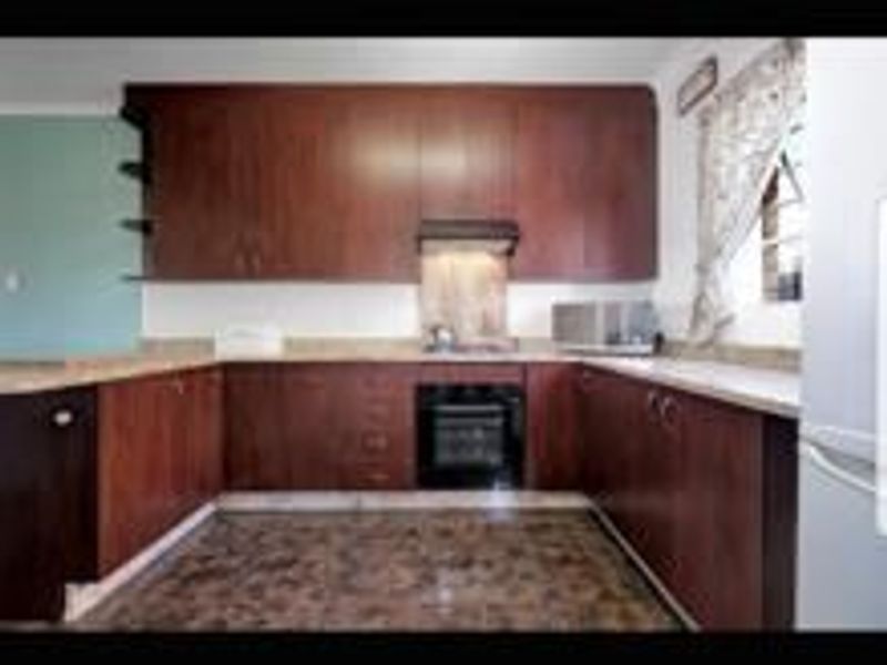 A U-shaped kitchen featuring dark wood cabinetry, integrated oven and hob, and stone countertops.