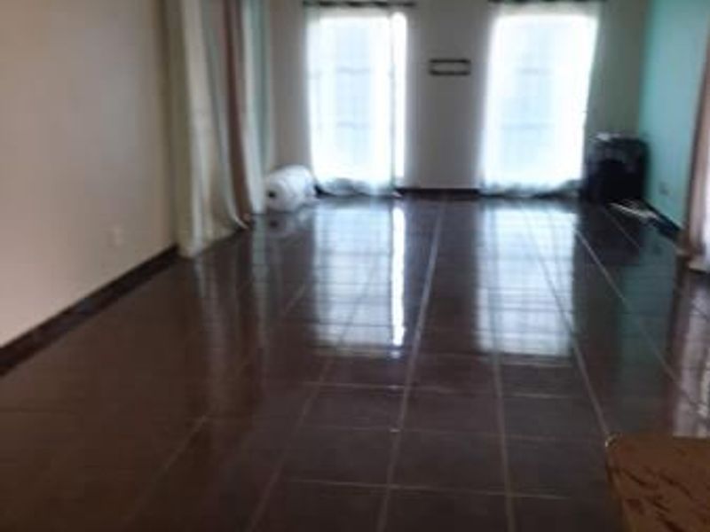 Spacious, empty living area featuring dark tiled flooring, an air conditioning unit, and large sliding glass doors providing natural light.