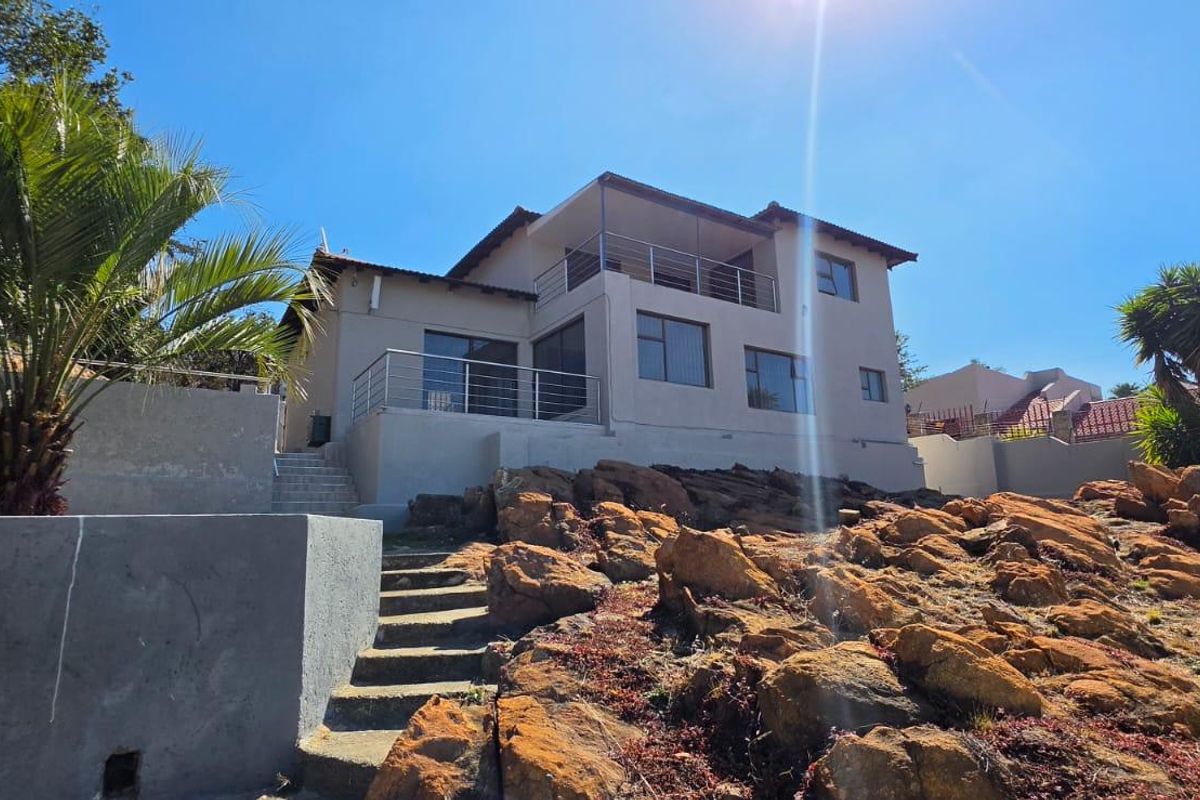 Rear view of a multi-level residential property featuring a balcony, terrace, and concrete stairs set against a natural rocky landscape.