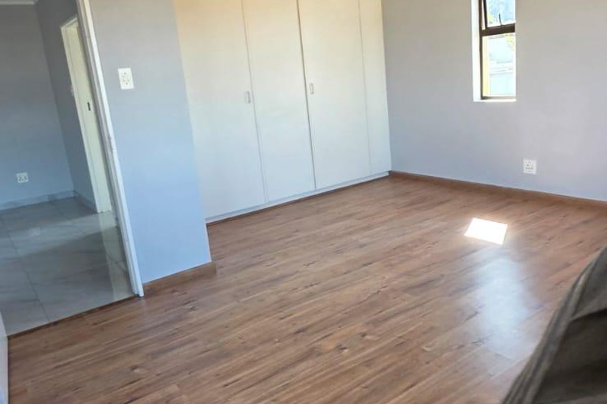 A spacious, empty bedroom featuring neutral grey walls, laminate wood flooring, and built-in storage cupboards.