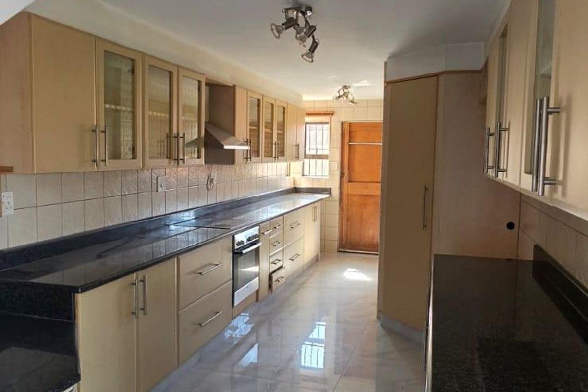 Spacious kitchen featuring granite countertops, ample built-in cabinetry, integrated oven, extractor fan, and modern tiled flooring.