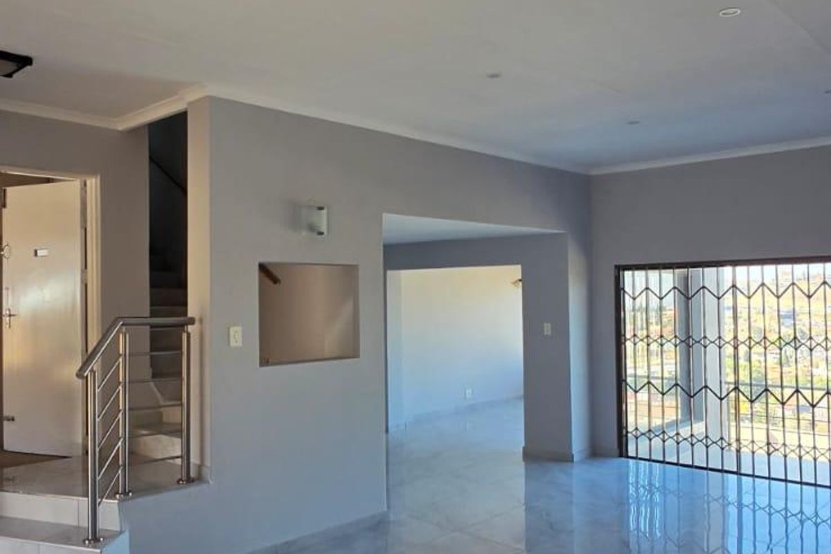 Spacious, open-plan living area featuring polished marble-look floor tiles, recessed lighting, and a modern staircase with stainless steel balustrades.