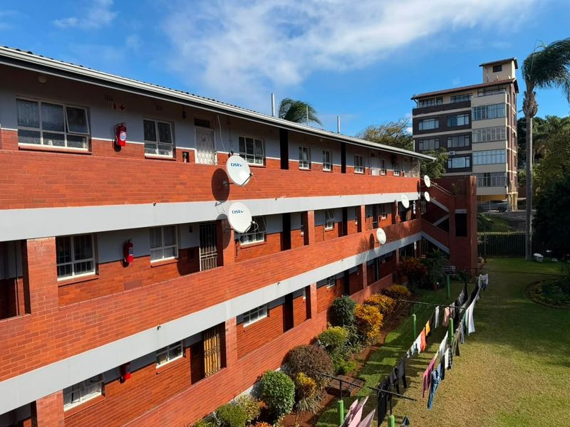 Exterior view of a multi-story apartment building featuring face brick construction, external walkways, and communal garden space.