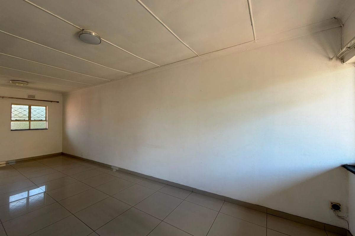 A spacious, empty living area featuring neutral tiled flooring, white walls, and ceiling-mounted lighting, providing a blank canvas for interior design.
