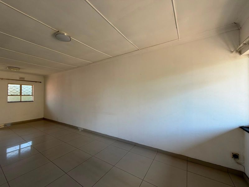A spacious, empty living area featuring neutral tiled flooring, white walls, and ceiling-mounted lighting, providing a blank canvas for interior design.