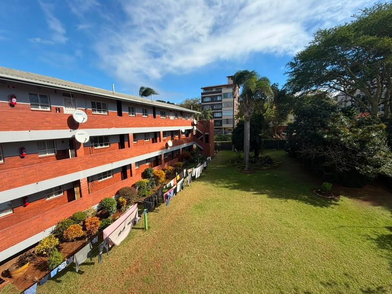View of the apartment building's rear brick facade overlooking a well-maintained communal garden area.