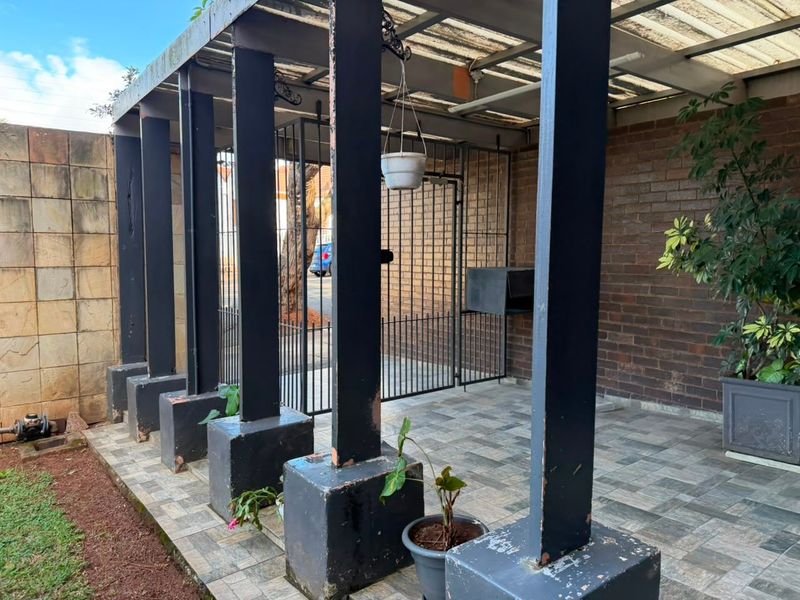 A covered patio area featuring a pergola structure, paved flooring, and secure metal gate access, providing a functional outdoor space.