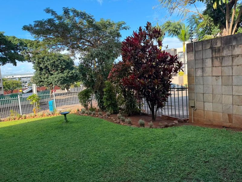 A well-maintained private garden area featuring a manicured lawn, established shrubs, and a secure stone-clad boundary wall with integrated electric fencing.