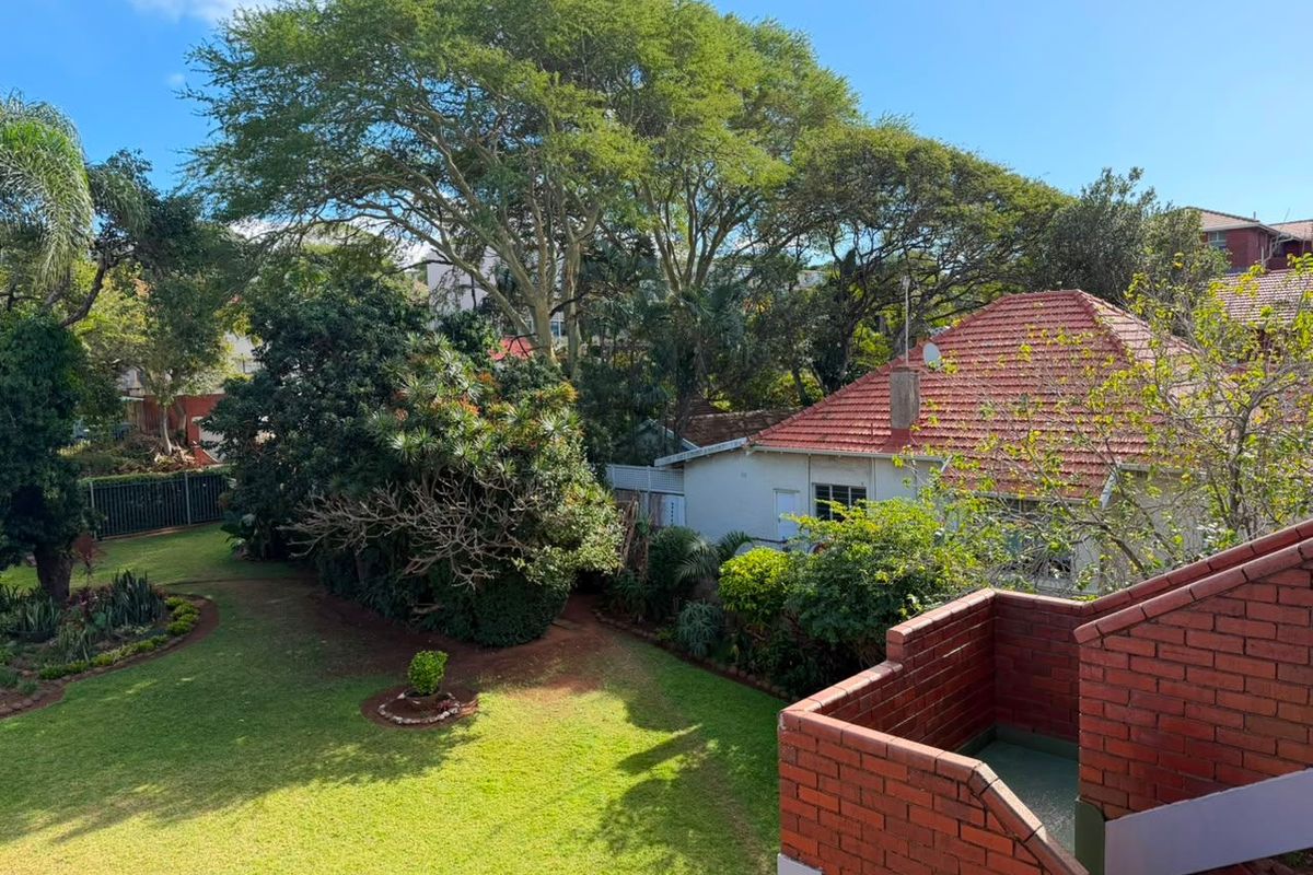 Elevated view of a private rear garden featuring a brick balcony and mature trees, providing a peaceful outdoor setting.