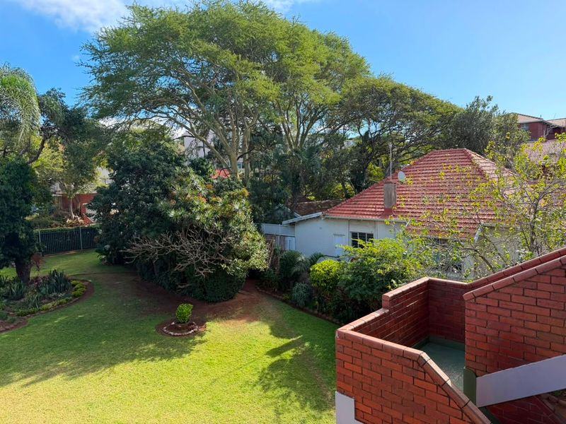 Elevated view of a private rear garden featuring a brick balcony and mature trees, providing a peaceful outdoor setting.