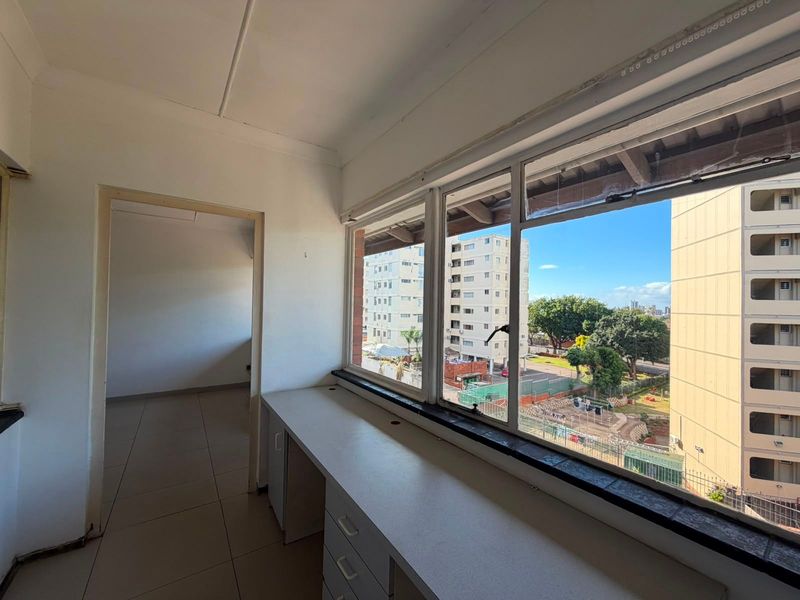 A compact utility space or study area featuring a built-in desk, tiled flooring, and large windows offering an urban view.