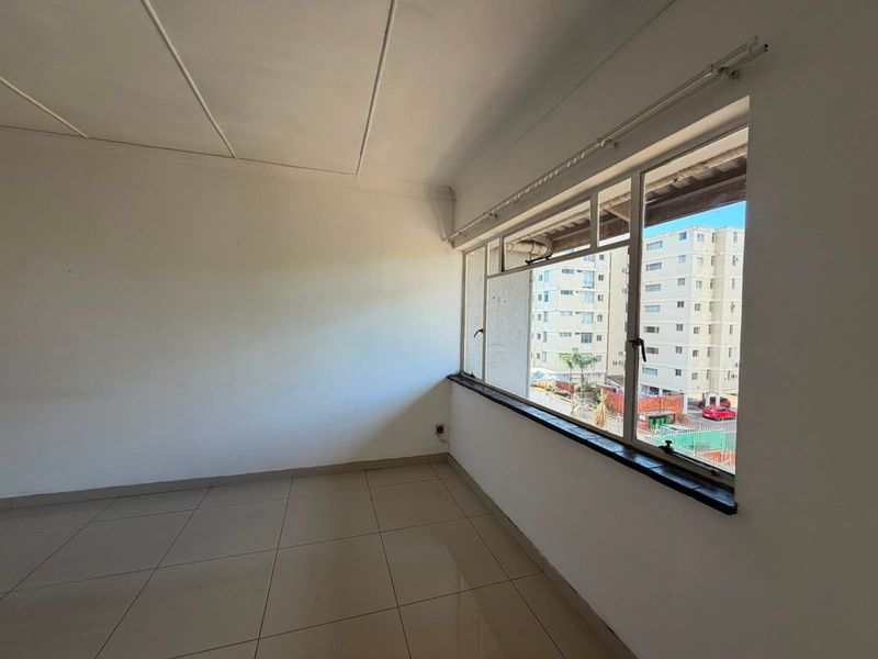 A bright, empty living area featuring neutral tiled flooring and large windows that provide ample natural light and an urban view.