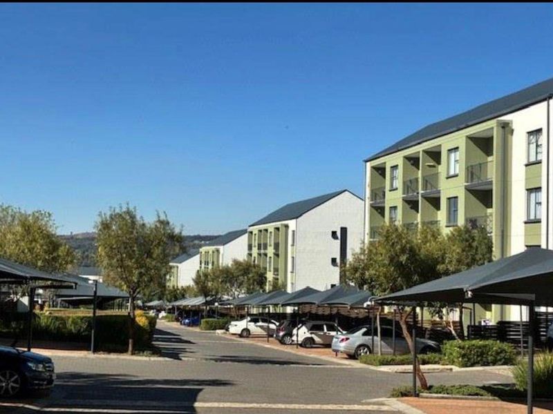 Exterior view of a modern apartment complex featuring paved driveways, covered parking bays, and well-maintained multi-story residential buildings.