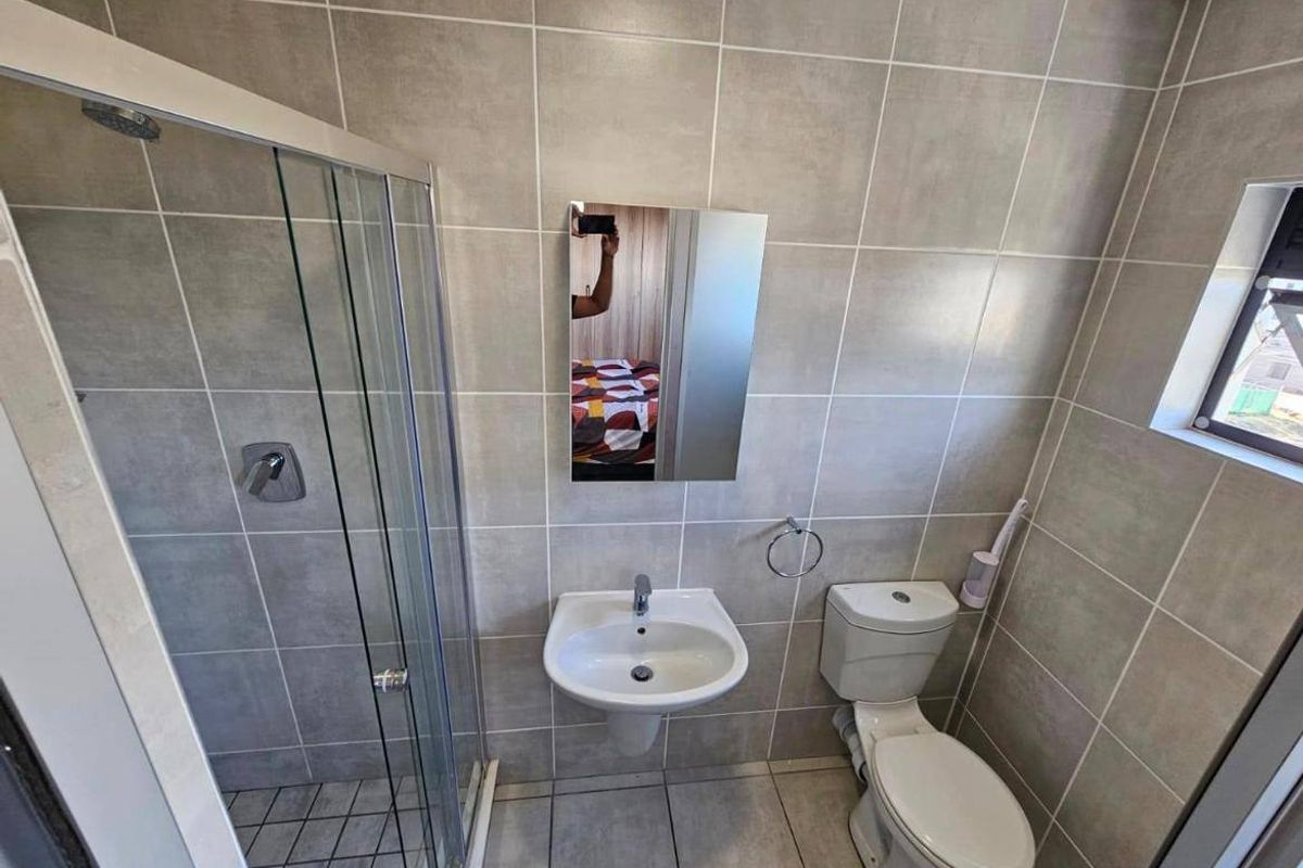 A clean, modern bathroom featuring a glass shower enclosure, wall-mounted basin, toilet, and neutral floor-to-ceiling tiling.