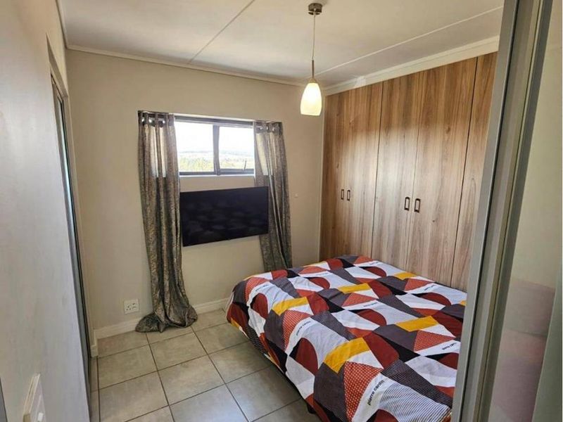 A compact bedroom featuring tiled flooring, built-in wooden cupboards, and a pendant light fixture.