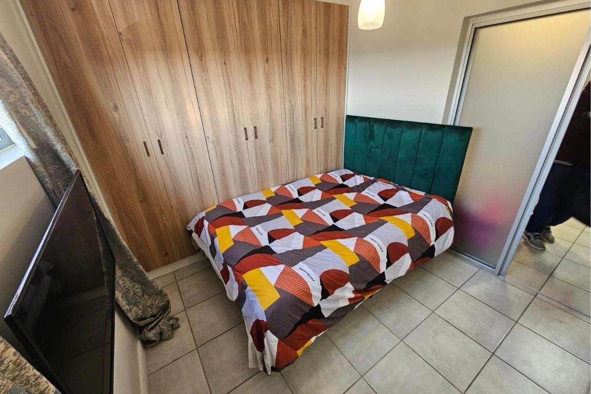 A well-maintained bedroom featuring modern wood-finish built-in cupboards, neutral tiled flooring, and a frosted glass sliding door.