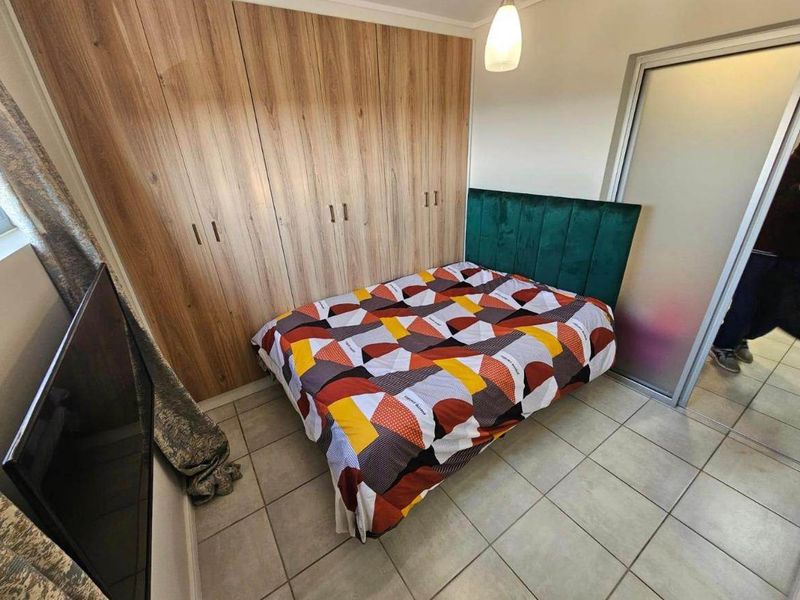 A well-maintained bedroom featuring modern wood-finish built-in cupboards, neutral tiled flooring, and a frosted glass sliding door.