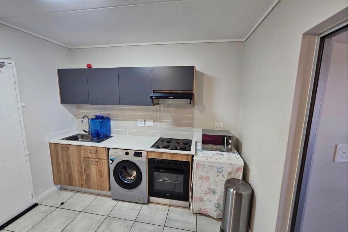 Compact kitchen featuring modern wood-grain and dark grey cabinetry, integrated oven and hob, tiled backsplash, and tiled flooring.